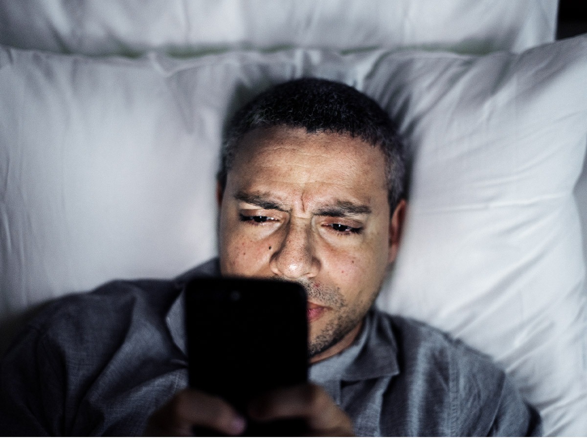 Man in bed on smartphone adjusting his smart home.